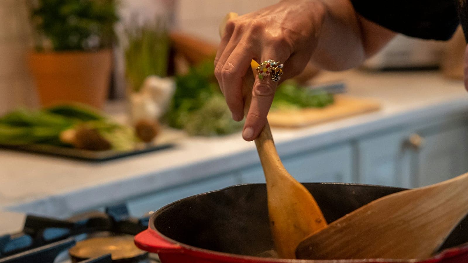 Una mano mescola con un cucchiaio di legno in una casseruola rossa sul fornello