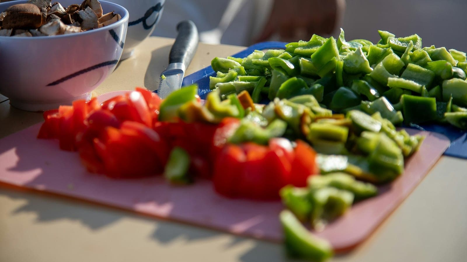 Peperoni rossi e verdi tagliati a cubetti su un tagliere, con una ciotola di funghi
