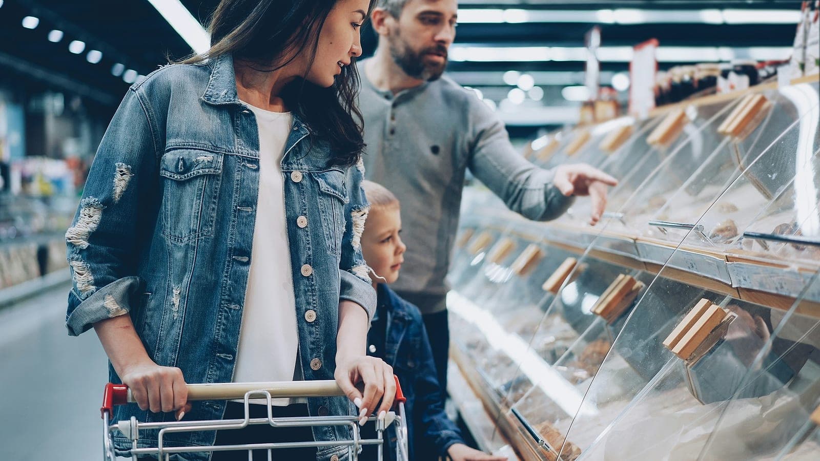 Una coppia con un bambino sceglie al banco del supermercato, lei spinge il carrello