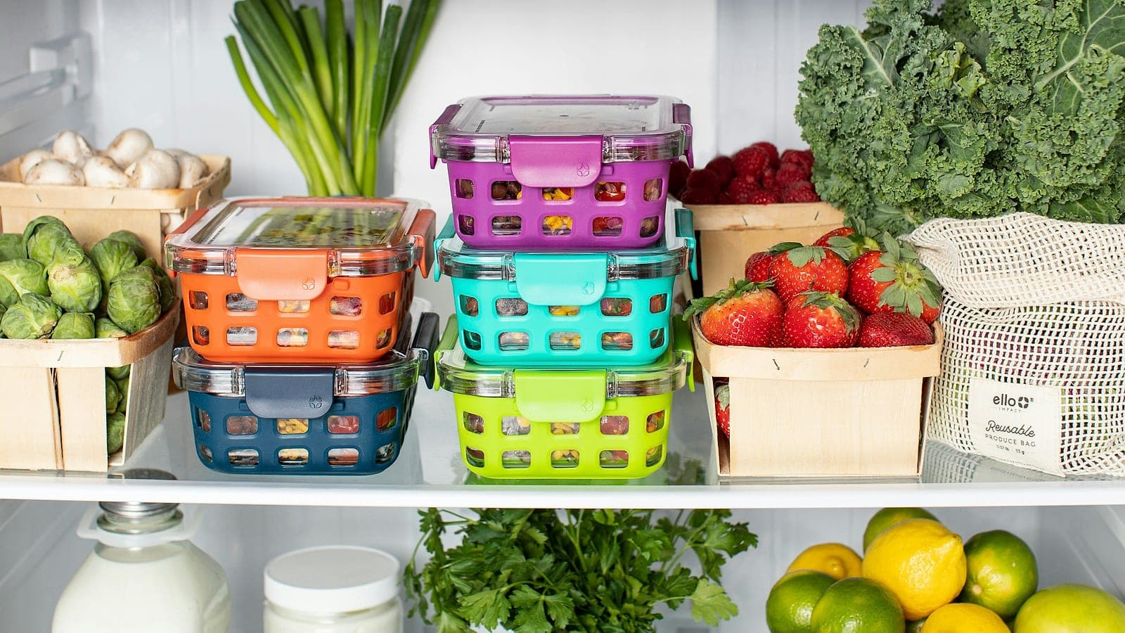 Contenitori colorati per alimenti impilati in frigorifero, fra fragole, cavolo riccio e altre verdure